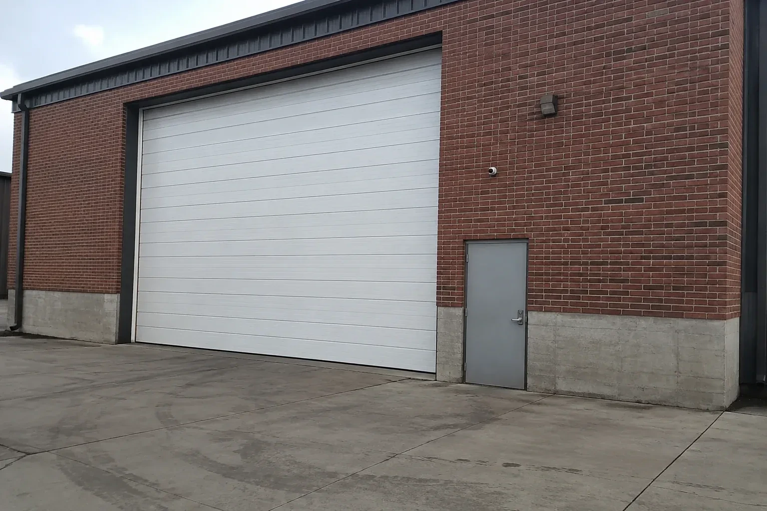 Tall closed sectional loading door beside a personnel door at a brick unit. — Commercial Sectional Door Repair, Toronto
