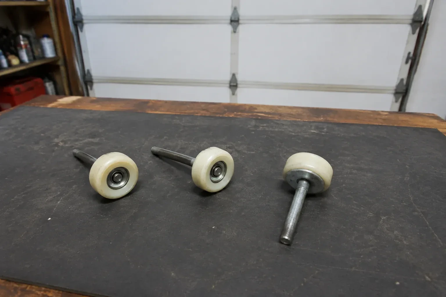Three detached nylon-wheel garage door rollers with steel stems on a work mat. — Garage Door Roller Replacement, Toronto